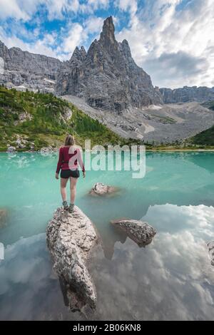 Junge Frau, Wanderer auf Felsen im Wasser am türkisgrünen Sorapis-See, Lago di Sorapis, Berggipfel Dito di Dio, in den Bergen, in den Bergen, Belluno Stockfoto