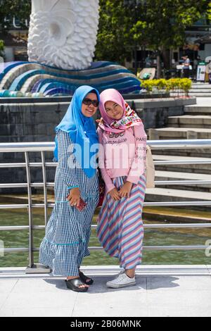 Zwei indonesische muslimische Frauen mehrerer Generationen, die einen schönen hellen Hijab tragen, posieren vor dem Merlion in Singapur. Stockfoto