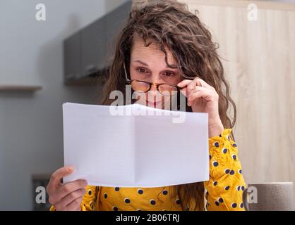 Eine ernsthafte Frau, die zu Hause auf erhaltene Post blickt Stockfoto