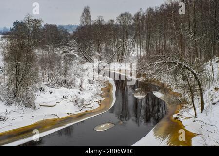 Blick auf den nicht gefrorenen Fluss. Winterlandschaft. Schnee auf dem Boden und Bäume. Bewölkter Tag. Stockfoto