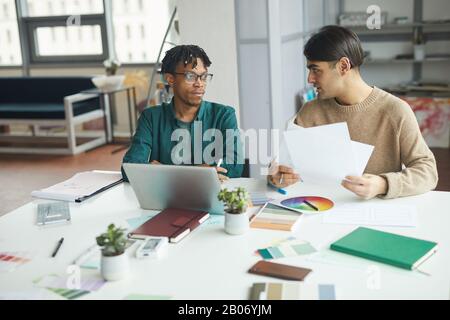 Zwei junge Designer sitzen mit Mustern am Tisch vor dem Laptop und diskutieren gemeinsam im Büro über ein neues Projekt Stockfoto