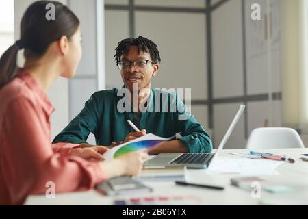 Junge Geschäftsleute sitzen am Tisch und diskutieren gemeinsam während ihrer Teamarbeit im Büro über Farbpalette Stockfoto