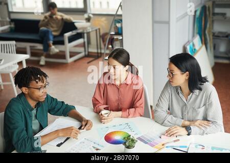 Gruppe junger Designer, die mit farbigem Muster am Tisch sitzen und während des Meetings im Team über das Projekt diskutieren Stockfoto