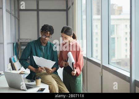 Zwei Geschäftspartner, die im Büro stehen und mit Geschäftsdokumenten arbeiten, die sie lesen und prüfen Stockfoto
