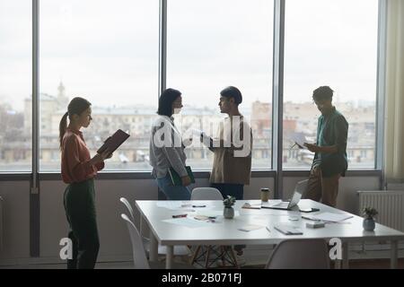 Gruppe junger Geschäftsleute, die vor einem großen Fenster stehen und im Büro arbeiten Stockfoto