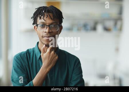 Junger afrikanischer Designer mit stilvoller Frisur und Brille, die im Büro auf die Kamera blickt Stockfoto