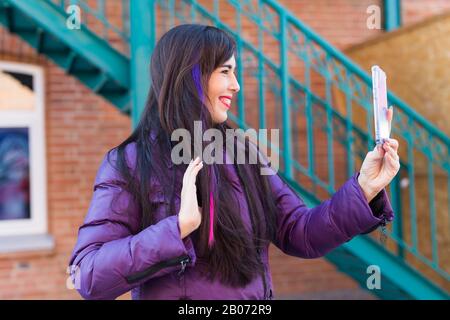 Technologien, Stadt- und Personen-Konzept - Hübsches Mädchen mit langen farbigen Haaren nimmt sich auf dem Dach eine selfie. Stockfoto