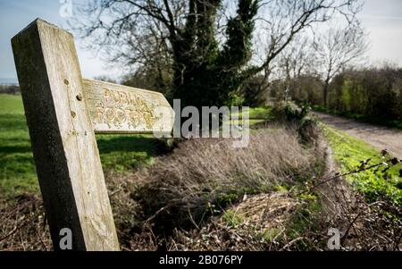 Englisches Schild für den öffentlichen Fußweg auf dem Land. Ein schiefes, mit Moos und Flechten bedecktes Schild, das Wanderer auf ihrer Route lenkt. Stockfoto
