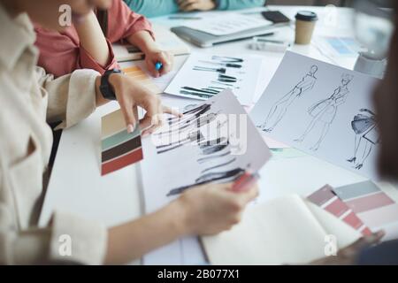 Nahaufnahme von Designern, die am Tisch sitzen und Modeskizzen von Kleidung während des Treffens im Büro untersuchen Stockfoto