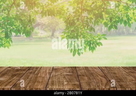 Holztisch oben auf verwackeln abstrakter grüner Baumgarten im Morgenhintergrund. Naturpark für Montage Produktdarstellung oder Design Key Visual Layout Stockfoto