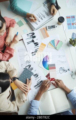 Nahaufnahme des Teams von Designern, die am Tisch sitzen und bei der Besprechung mit Modeskizzen von Kleidung im Team arbeiten Stockfoto