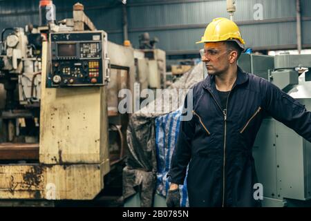 Portrait gutaussehender Arbeiter mit Sicherheitsanzug und alter Maschine im Werk. Stockfoto