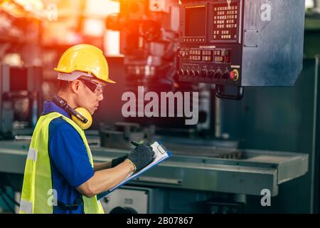 Asiatischer Ingenieur überprüft die Maschine im Werk, Arbeiter schreibt Notiz mit Listenpapier. Stockfoto