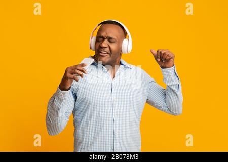 Emotionaler afrikaner reifer Mann im Kopfhörer, der am Telefon singt Stockfoto