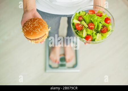 Diät Konzept, schöne junge Frau die Wahl zwischen gesunden Essen und Junk Food Stockfoto