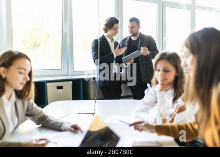 Geschultes Team von Grafikdesignern, das während des Arbeitsprozesses eine kreative Lösung entwickelt und gleichzeitig ein erfolgreiches Geschäftskonzept diskutiert, Stockfoto