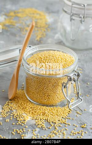 Rohe, trockene, gehullte Hirse in einem Glasbecher mit einem Löffel in der Nähe Stockfoto