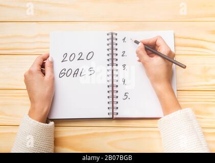 Weibliche Hände schreiben zukünftige 2020-Ziele in Spiralnotizblock Stockfoto
