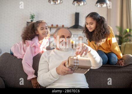 Bärtiger Mann im gestreiften Pullover, der die Geschenkbox für den Tag öffnet Stockfoto