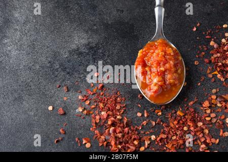 Traditionelle Adjika heiße Chili Pfeffersoße Paste Harissa im Löffel auf schwarz. Tunesien-Küche, georgische und arabische Küche. Nahaufnahme. Leerzeichen für Text. Stockfoto