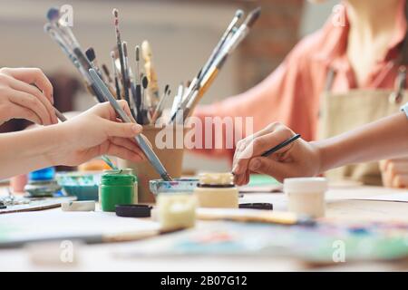 Nahaufnahme von Kindern mit Pinsel- und Aquarellfarben, um Bilder am Tisch zu malen Stockfoto
