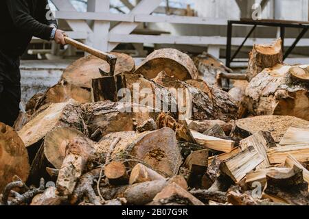 Mann hackt Holz mit Vintage-Axt. Details zu fliegenden Holzstücken auf Holzklotz mit Sägemehl. Stockfoto