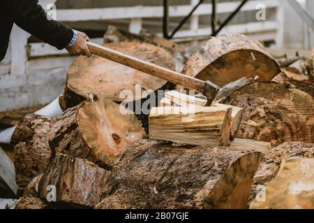 Mann hackt Holz mit Vintage-Axt. Details zu fliegenden Holzstücken auf Holzklotz mit Sägemehl. Stockfoto