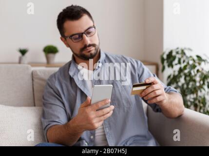 Konzentrierter junger Mann, der online mit Smartphone einkaufen geht Stockfoto