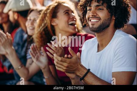 Mann klatscht beim Fußballspielen mit Freunden im Stadion. Multiethnische Gruppe von Freunden, die ein Fußballspiel im Stadion genießen. Stockfoto