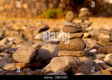 Balancierte Steinpyramide am Ufer des Ozeans im Morgengrauen. Der Turm mit Meeresschälchen steht für Stabilität, Zen, Harmonie und Gleichgewicht. Stockfoto