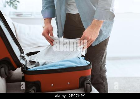 Reisekonzept. Kerl packt Kleidung in Koffer Stockfoto