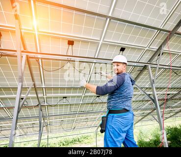 Junge Elektriker in Harthut und Gummihandschuhe verkabeln Solarfoto-Voltaic-Module innerhalb des neu installierten Panel-Systems an hellem, sonnigen Tag. Alternative Energie und profitables Investitionskonzept. Stockfoto