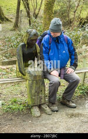 Walker saß auf dem Tarka Trail vor Great Torrington, Devon, England, und sah sich eine rustikale Holzskulptur einer Frau an Stockfoto