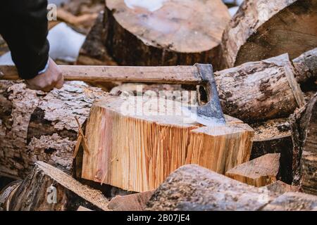 Mann hackt Holz mit Vintage-Axt. Details zu fliegenden Holzstücken auf Holzklotz mit Sägemehl. Stockfoto