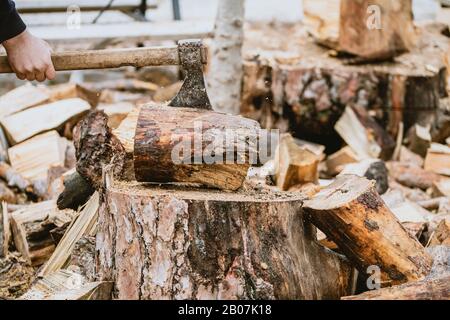 Mann hackt Holz mit Vintage-Axt. Details zu fliegenden Holzstücken auf Holzklotz mit Sägemehl. Stockfoto