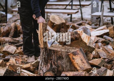 Mann hackt Holz mit Vintage-Axt. Details zu fliegenden Holzstücken auf Holzklotz mit Sägemehl. Stockfoto
