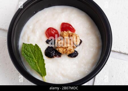 Milchporridge aus Reis mit Beeren und Butter zum Frühstück in schwarzem Lebensmittelbehälter, Draufsicht, Nahaufnahme Stockfoto