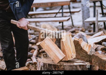 Mann hackt Holz mit Vintage-Axt. Details zu fliegenden Holzstücken auf Holzklotz mit Sägemehl. Stockfoto