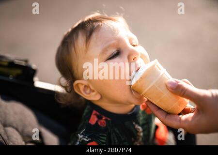 Mutter füttert Baby Kind Junge Eiscreme - Junge Mutter und ihr Baby essen weißes Vanille cremig Dessert - Sitzt in einem Babywagen Kinderwagen - kaukasische Familie 1 Stockfoto