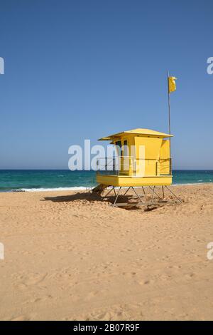 Hellgelbe Rettungsstation am Strand Corralejo, Fuerteventura mit weißem Sand, türkisfarbenem Atlantik und blauem Himmel. Stockfoto