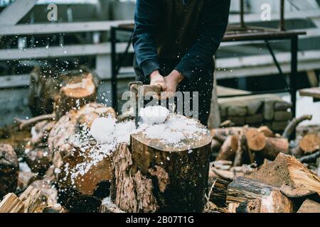 Mann hackt Holz mit Vintage-Axt. Details zu fliegenden Holzstücken auf Holzklotz mit Sägemehl. Stockfoto