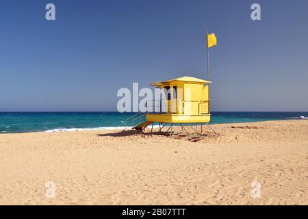 Hellgelbe Rettungsstation am Strand Corralejo, Fuerteventura mit weißem Sand, türkisfarbenem Atlantik und blauem Himmel. Stockfoto