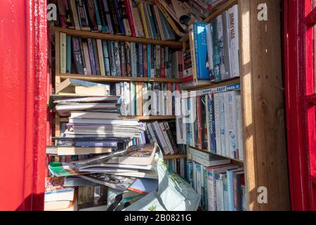 Bücher, die in der Old Red GPO Telephone Box an Der Straße, Barton Stacey, Winchester, Hampshire, England, Großbritannien - Bibliothek für Gemeinden gestapelt und gelagert wurden. Stockfoto