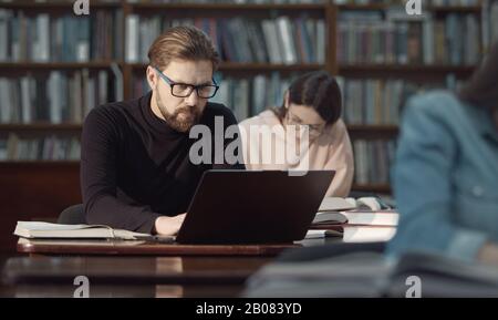 Mann, der in der Bibliothek einen Laptop arbeitet Stockfoto