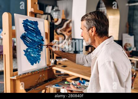 Begeisterter Künstler, der in seinem Studio auf Leinwand arbeitet Stockfoto