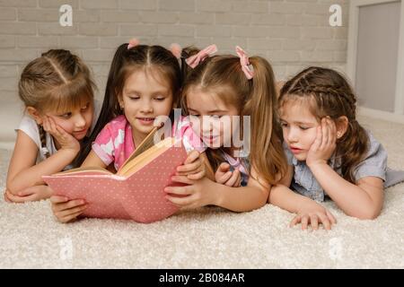 Die Gruppe der Kinder legte sich auf den Boden und las das Märchenbuch. Vier kleine Mädchen studierten zusammen in der Klasse. Freundschaftskonzept Stockfoto