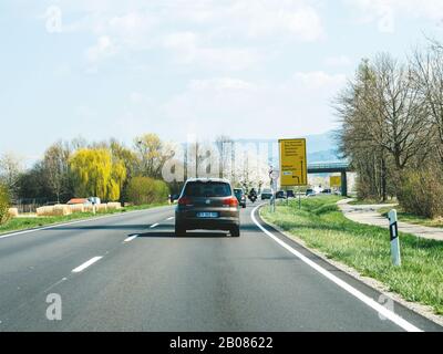 Deutschland - 31. März 2019: Rückansicht des braunen Volkswagen Tiguan SUV, der auf der Landstraße mit schwarzen Waldbergen im Hintergrund schnell fährt Stockfoto