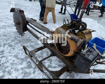 Dieses Foto stammt vom 16. Februar 2020 und wurde in South Bristol, Maine, auf dem Ice Harvest Festival in Thompson Pond aufgenommen. Es zeigt die Eisschneidemaschine, mit der sie die ersten Schnitte im Eis machen, um die Blöcke zu markieren. Sägen werden verwendet, um das Eis zu durchschneiden. Freiwillige sammeln sich, um Eis aus dem Teich zu schneiden, wie sie es in den 1820er Jahren an diesem Standort hatten. Das Gelände wurde in den 1980er Jahren geschlossen. Heute verwenden sie dieselben Geräte, die in der Vergangenheit verwendet wurden. Das Eis war in erster Linie für den lokalen Verbrauch bestimmt. Jetzt werden die Eisblöcke aufbewahrt und verwendet, um Eis für die jährliche Eiscreme Social im Sommer zu machen. Stockfoto