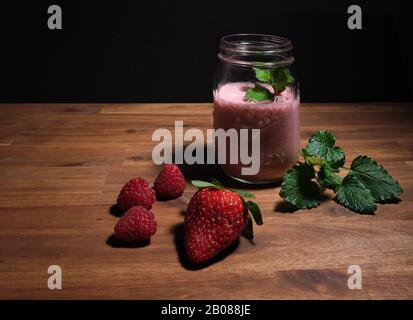 Erdbeer-Smoothie auf einer Holzplatte mit schwarzem Hintergrund, Werbefläche Stockfoto