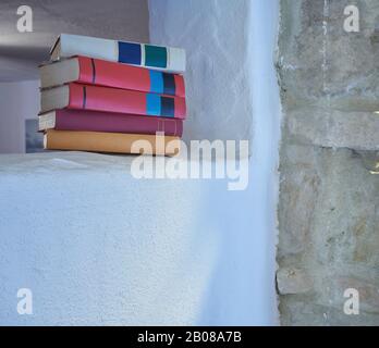 Fünf gestapelte Bücher, die in einem hohen Raum in Wandbuchtiteln platziert sind, rechtwinklig, innen, offene Fläche, weißes Wandstudio, rustikale Steinwand Stockfoto